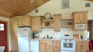 Una cocina con armarios de madera, un refrigerador, un microondas y un reloj en la pared.