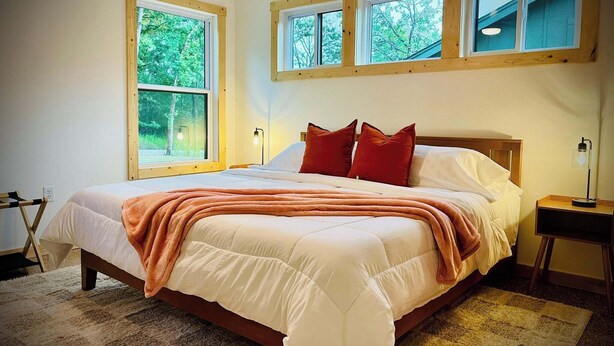 Un dormitorio con una cama grande, varias ventanas y una mesita de noche con lámpara.