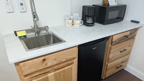 Una cocina compacta con pileta, muebles de madera, lavavajillas, microondas y cafetera.