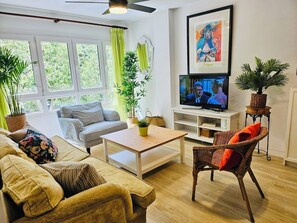 A living room with a sofa, armchair, TV, and potted plants. - Central and comfortable location! 2 comfortable double beds. Free parking. (Málaga)