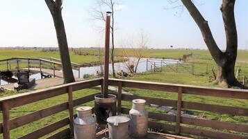 A wooden deck with metal containers and a grill, overlooking a grassy area and a body of water.