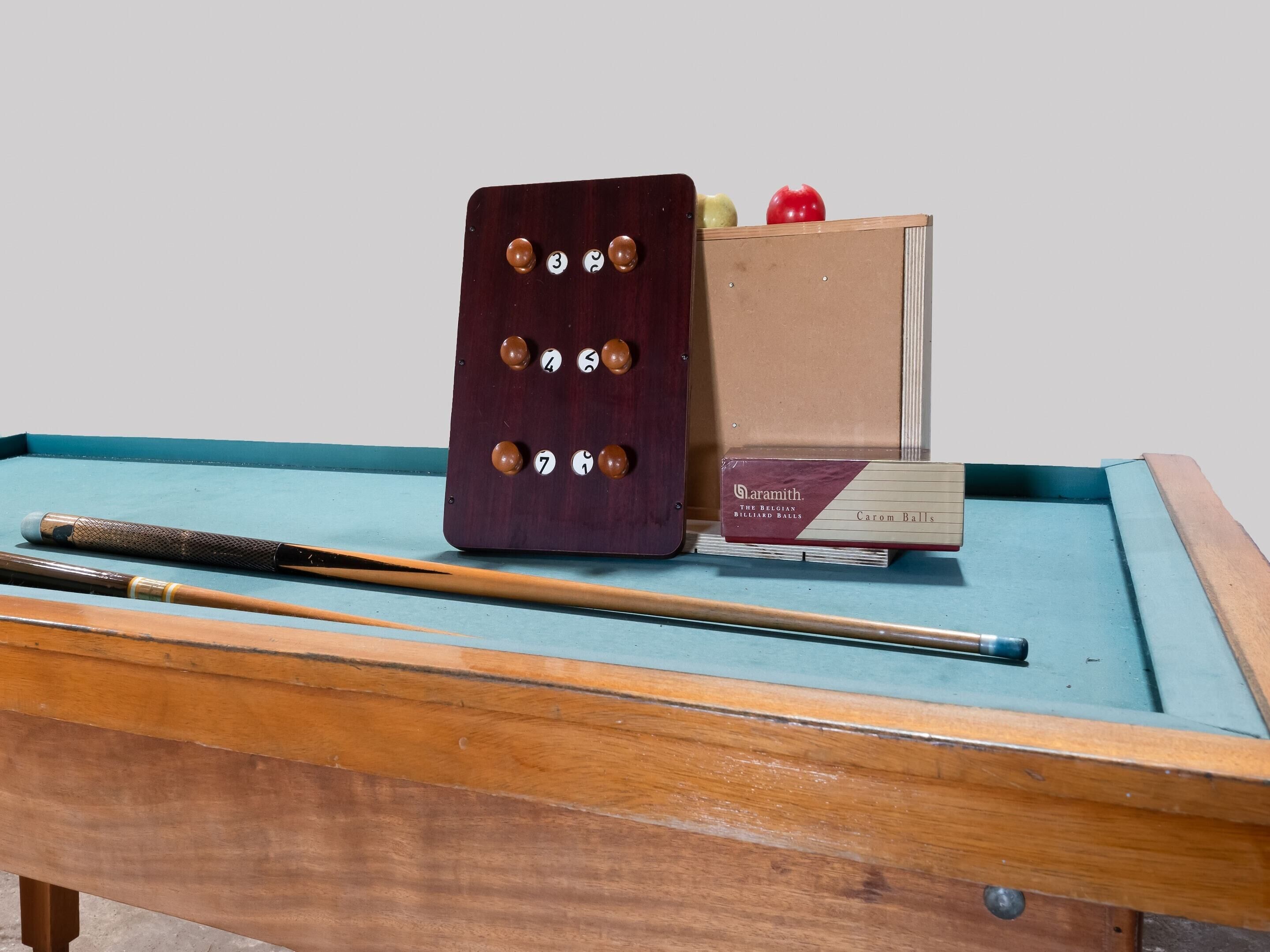 Une table de billard avec une queue, un jeu de billes et une boîte étiquetée « Daramith ».