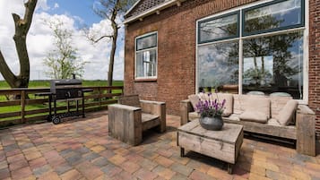 A patio with a wooden bench, a table with a flower pot, and a barbecue grill.