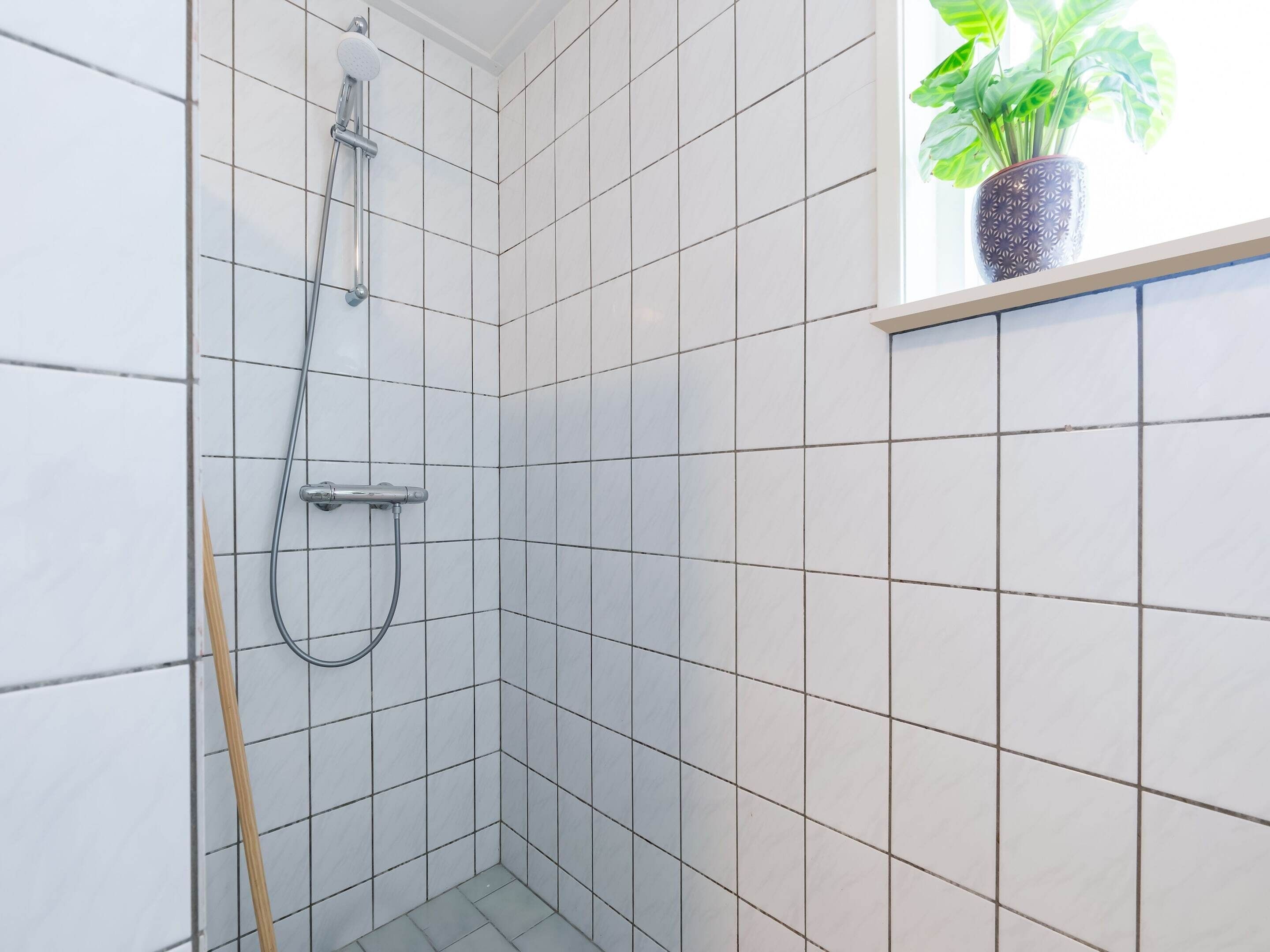 A small, tiled shower area with a handheld showerhead and a handheld shower attachment.