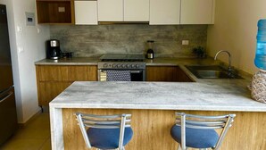 A modern kitchen with wooden cabinets, a built-in oven, a coffee maker, and a sink.
