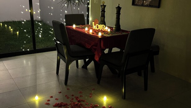 A dining area with a table set for two, adorned with candles and rose petals.