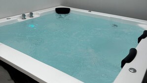 A rectangular hot tub with a white interior and a black seat, set against a plain wall.