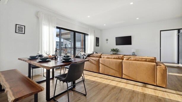 A modern living room with a wooden dining table, a sofa set, and a flat-screen TV mounted on the wall. - The Crystal Palace 2, pet friendly 2 bedroom apartment (Jindabyne)