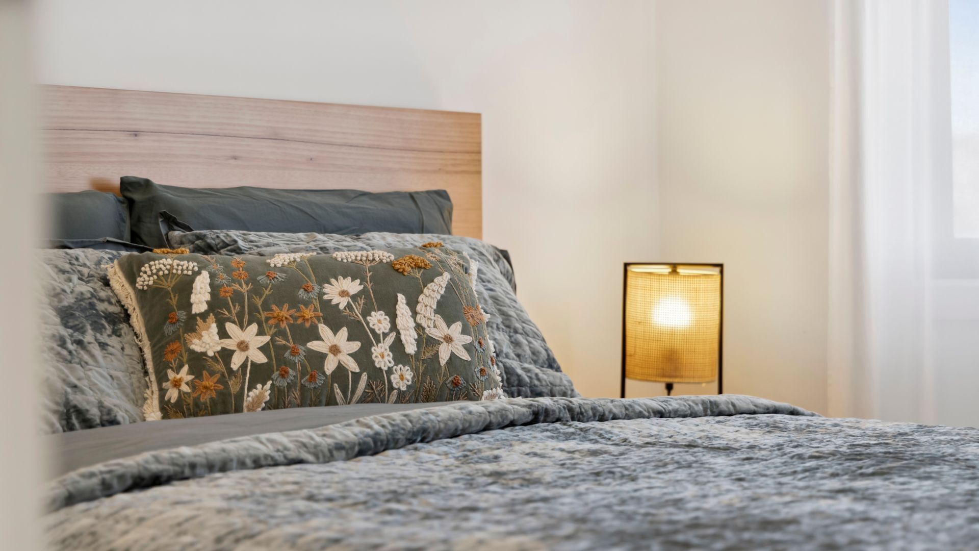 A bedroom with a bed, pillows, a nightstand, and a lamp.