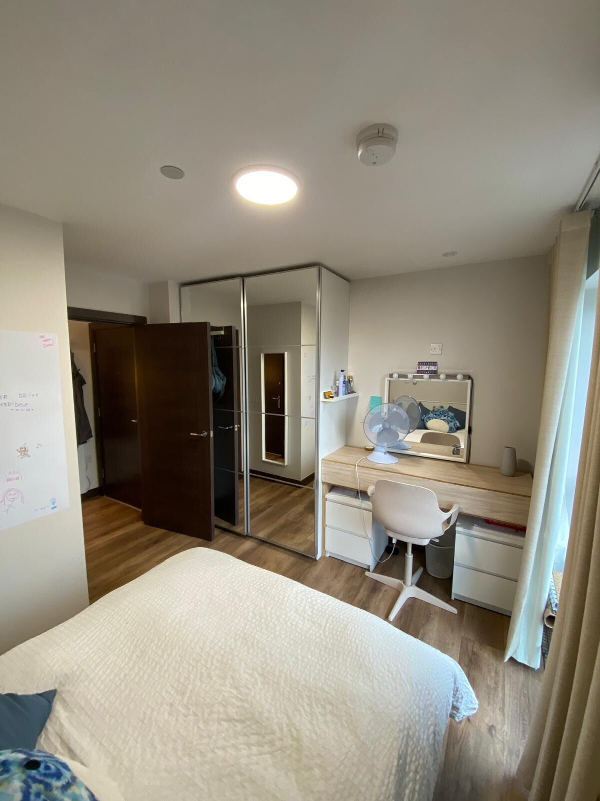 A bedroom with a bed, a desk with a chair, a mirror, and a wardrobe.