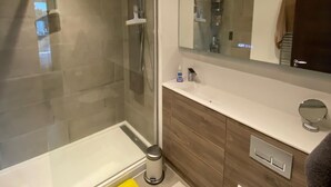 A modern bathroom with a glass shower enclosure, a white sink, a mirror, and wooden cabinetry.