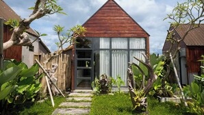 A house with a triangular roof, a wooden fence, and a garden with various plants. - Kose Villa Ubud (Ubud)