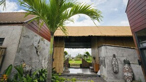 A traditional building with a thatched roof entrance, a palm tree, and decorative wall carvings. - Kose Villa Ubud (Ubud)
