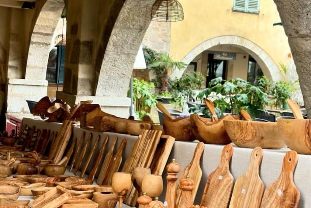 Une variété d’ustensiles de cuisine en bois, exposés dans un décor extérieur agrémenté d’arches et de plantes.