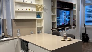 Moderni keittiö, jossa on valkoiset kaapit, keskellä oleva keittiösaareke ja sisäänrakennettu televisio.