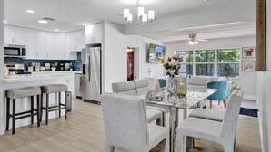 A modern kitchen with white cabinets, a stainless steel refrigerator, and a glass dining table with grey chairs. - Dania Beach 4BR • Pool • Game Room • Discounted! (Dania Beach)