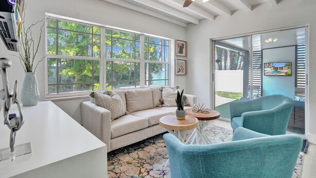 A modern living room with a sofa, two chairs, a coffee table, and a ceiling fan. Large windows provide a view of greenery outside. - Dania Beach 4BR • Pool • Game Room • Discounted! (Dania Beach)