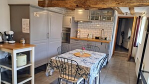Cocina compacta con armarios blancos, horno integrado y cafetera.