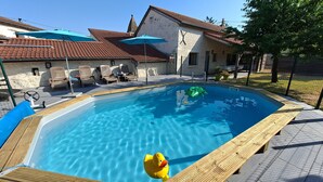 Una piscina con muelle de madera, sillas de descanso y puesto de socorrista.