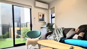 A modern living room with a sofa, a chair, a coffee table, and a sliding glass door leading to a garden.