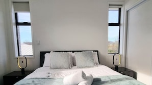 A bedroom with a bed, two bedside tables, a window, and a view of the outside.