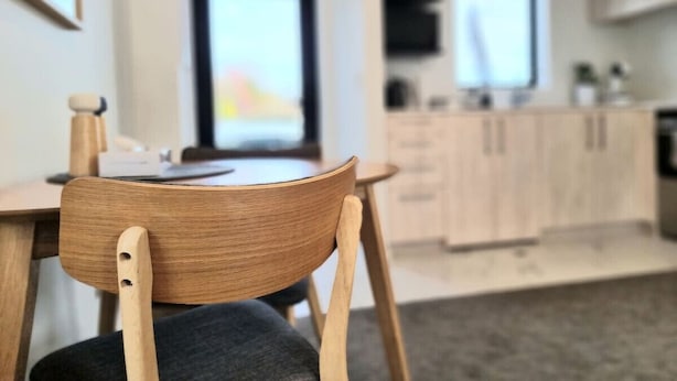 A modern kitchen with wooden cabinets and a dining area with a wooden chair.