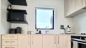 A modern kitchen with light wood cabinets, a black microwave, a window, and a stove.