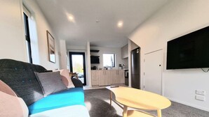 A modern living room with a sofa, a small table, and a kitchen in the background.