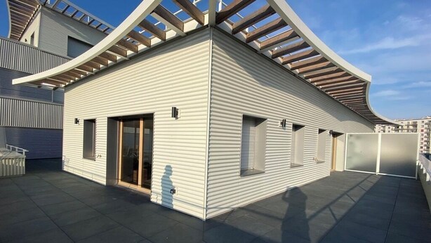 A modern building with a flat roof, large windows, and a covered outdoor area.