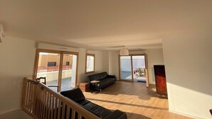 A spacious living area with a wooden floor, a black sofa, a small table, and a large window with a view of a building.