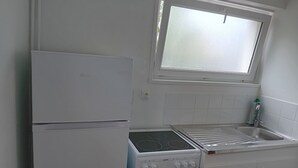 A compact kitchen with a white refrigerator, stove, and oven, a window above the sink, and white tiled walls. - Vacation studio in private house. (Concarneau)