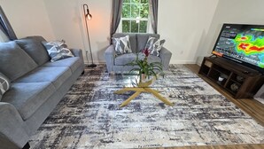Ein Wohnzimmer mit grauem Sofa, einem Couchtisch mit Pflanze und einem Fernseher, der einen Wetterradar anzeigt.