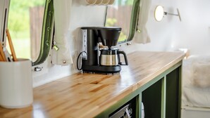 Een kitchenette met een koffiezetapparaat, een raam met gordijnen en een bekerhouder.
