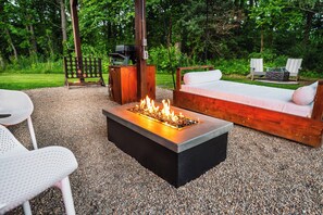 Feuerstelle mit einer hölzernen Bank und zwei Adirondack-Stühlen in einem Garten.