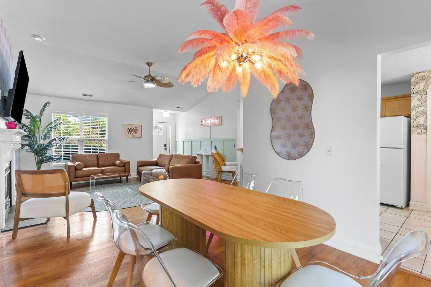 A modern living room with a wooden dining table, clear chairs, a ceiling fan, and a unique feather-like light fixture.