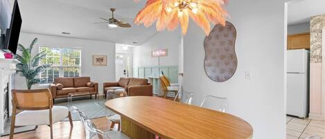 A modern living room with a wooden dining table, clear chairs, a ceiling fan, and a unique feather-like light fixture.