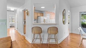 A modern kitchen with white cabinets, a white refrigerator, and a wooden countertop. There are two wicker chairs in front of the kitchen. - The Salty Flamingo w Pool+Hot Tub+Ping Pong (Murrayville)