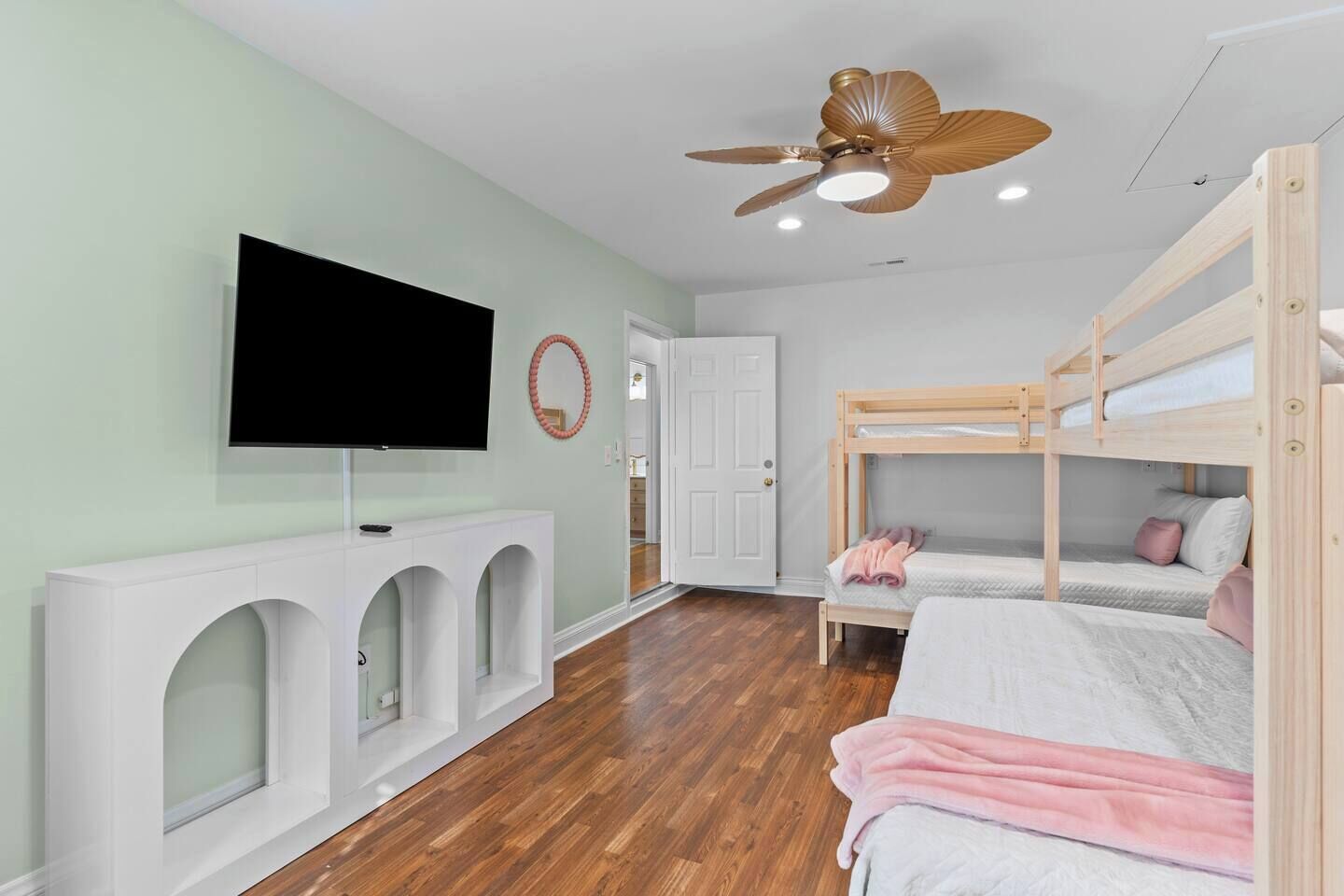 A bedroom with bunk beds, a TV, a ceiling fan, and a white console table.