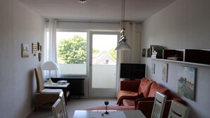 Ein kleiner, heller Raum mit Esstisch, Stuhl, Sofa und Fernseher.