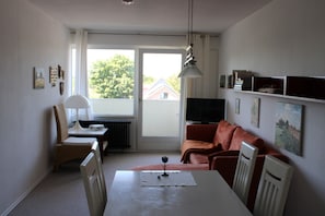 A small, bright room with a dining table, a chair, a sofa, and a television.