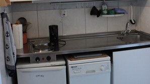 Eine kompakte Küche mit weißen Schränken, einer kleinen Arbeitsfläche, einer Kaffeemaschine, einem Minikühlschrank und einem Geschirrspüler.