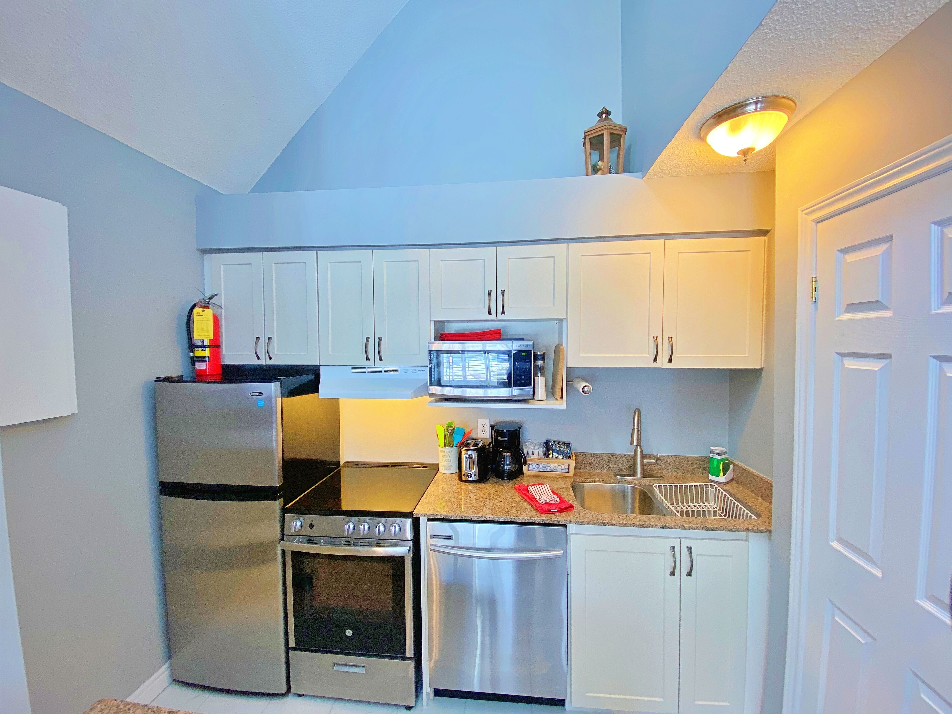 Una cocina compacta con armarios blancos, electrodomésticos de acero inoxidable, microondas y cafetera.