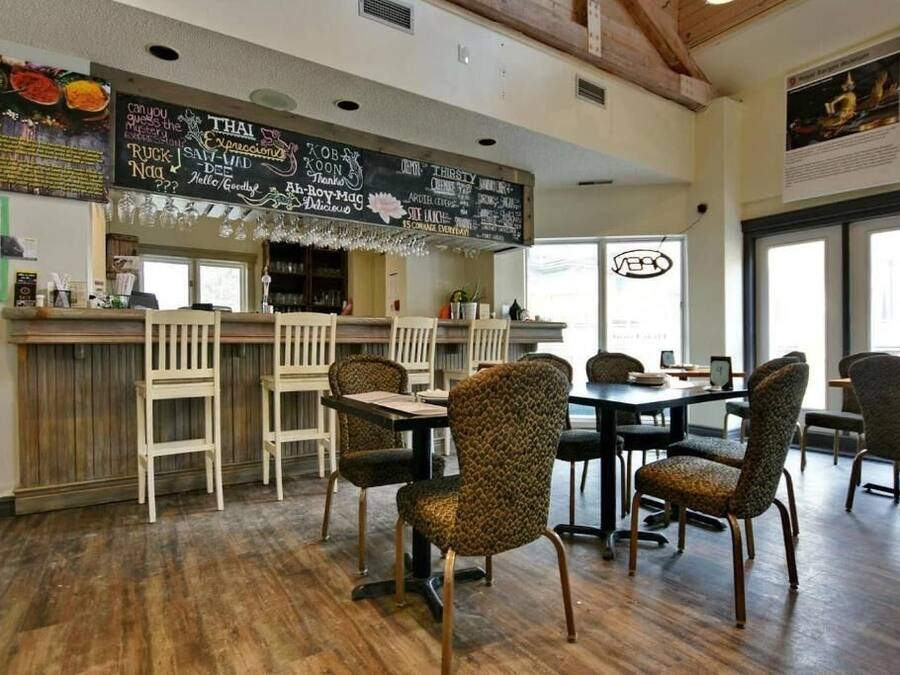 A restaurant interior with a wooden bar, patterned chairs, and a chalkboard menu.