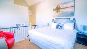 Quarto de hotel com uma cama grande, uma cadeira vermelha, um quadro de um pôr do sol e vista para o exterior.
