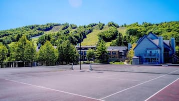 An outdoor tennis court with a net, surrounded by trees and buildings.