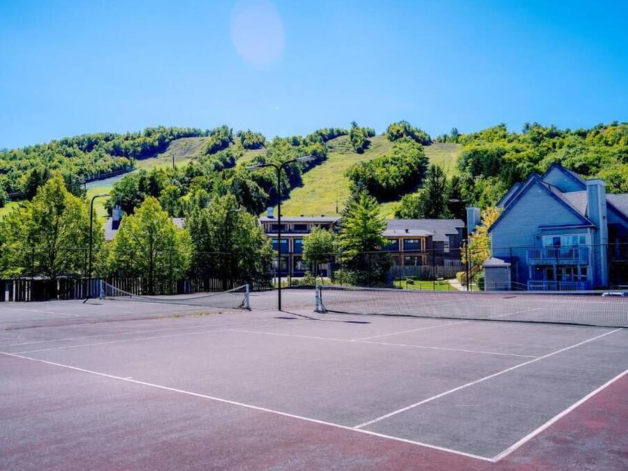 An outdoor tennis court with a net, surrounded by trees and buildings.