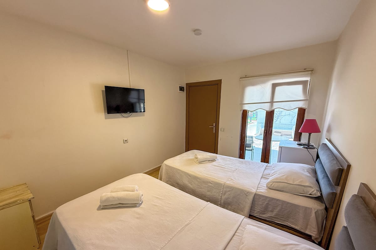 Una habitación de hotel con dos camas, televisor, ventana con cortinas y lámpara.