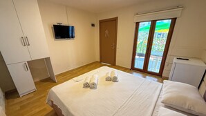 A bedroom with a bed, a television, a wardrobe, and a sliding door to a balcony. - Address Küçükkuyu (Ayvacik)