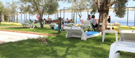 An outdoor seating area with white plastic chairs and tables, some with numbers, near a body of water and trees.