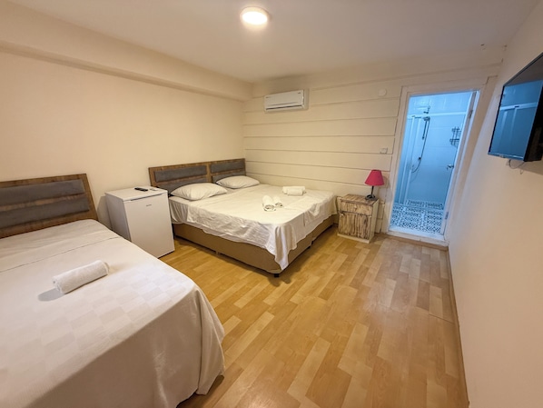 A bedroom with two beds, a small bedside table, a heater, and a shower area. - Address Küçükkuyu (Ayvacik)